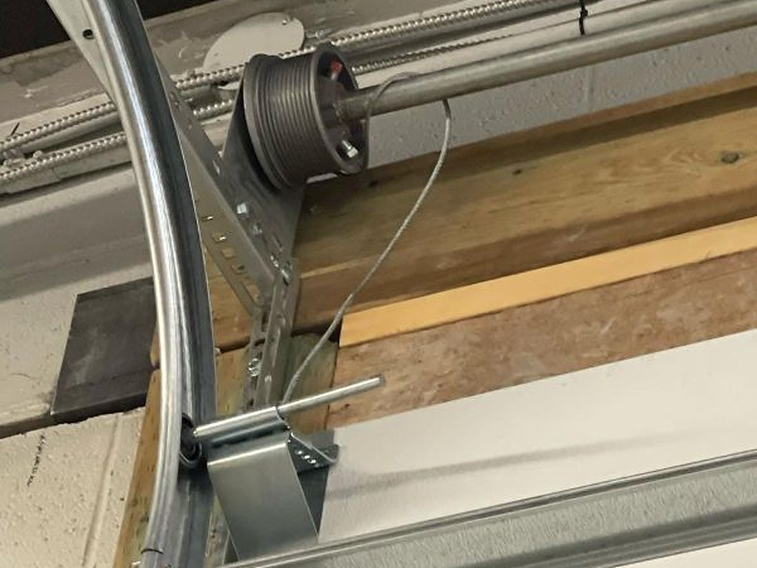 Lift cable and cable drum at the top corner of a garage door, the curved track above and the cable running down to the bottom bracket