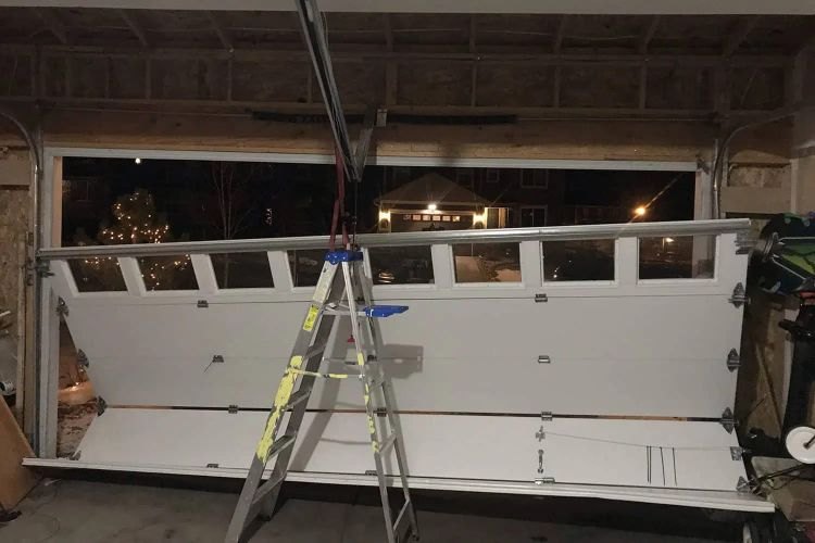 Sectional garage door lifted clear of its tracks and propped on a stepladder inside the garage during a night call, with the open doorway behind it