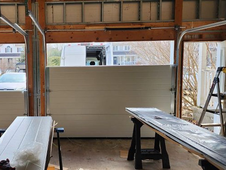 New insulated garage door part way through installation, remaining sections staged on trestles inside the garage