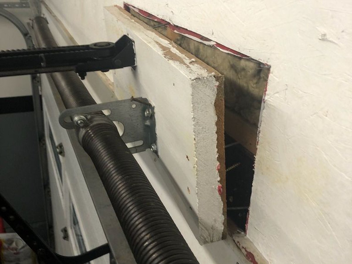 Header wall opened up beside a torsion spring to reach the structural backing behind the anchor bracket